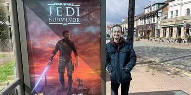 Graduate Max McGuire stood to the right of a large promotional poster for Star Wars Jedi: Survivor