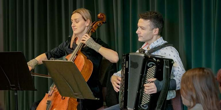 A woman playing cello sat next to a man playing accordion