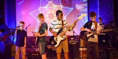 A pop band of young musicians approximately 9-13 years old perform on stage