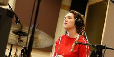 Abbie Finn - Female drummer at kit wearing headphones and a red top