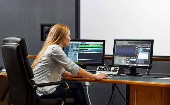 Student in Film Music studio with large projection screen, sat using digital audio software and professional music studio equipment.